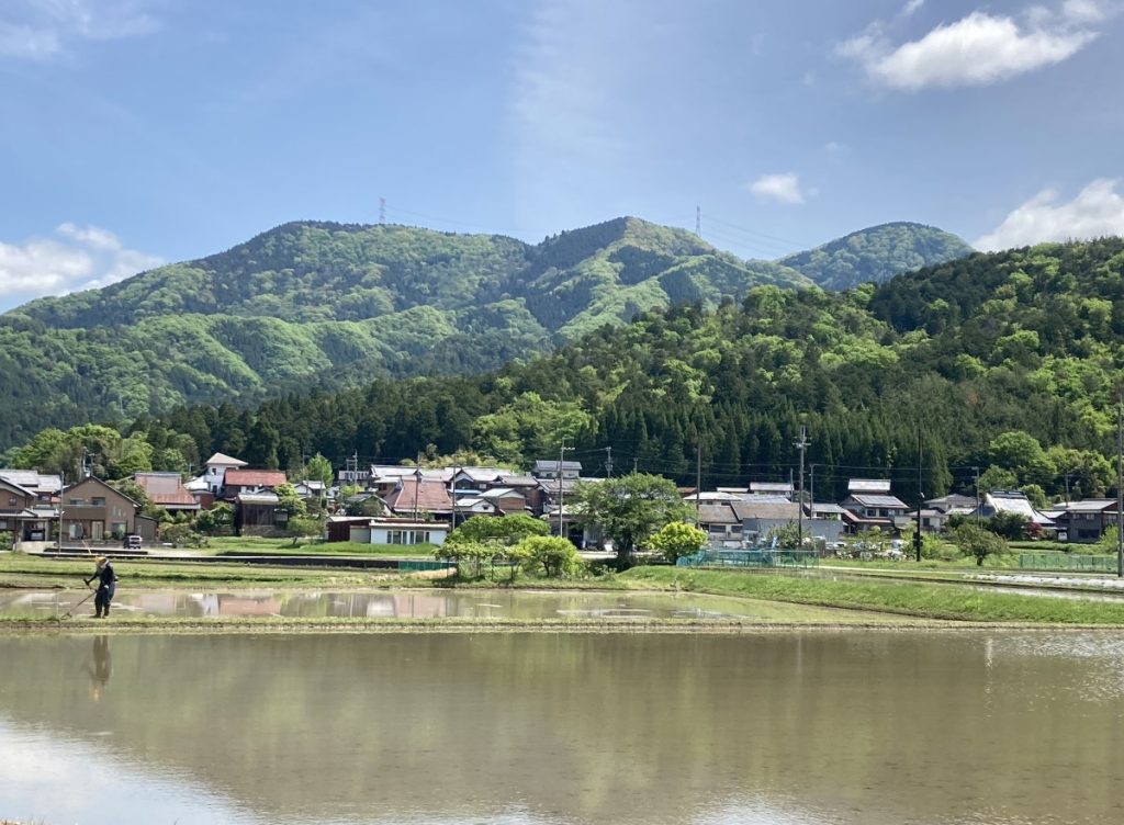 水を張った田植え前の田んぼ・集落・新緑の山（2024.5.2多賀町大岡）